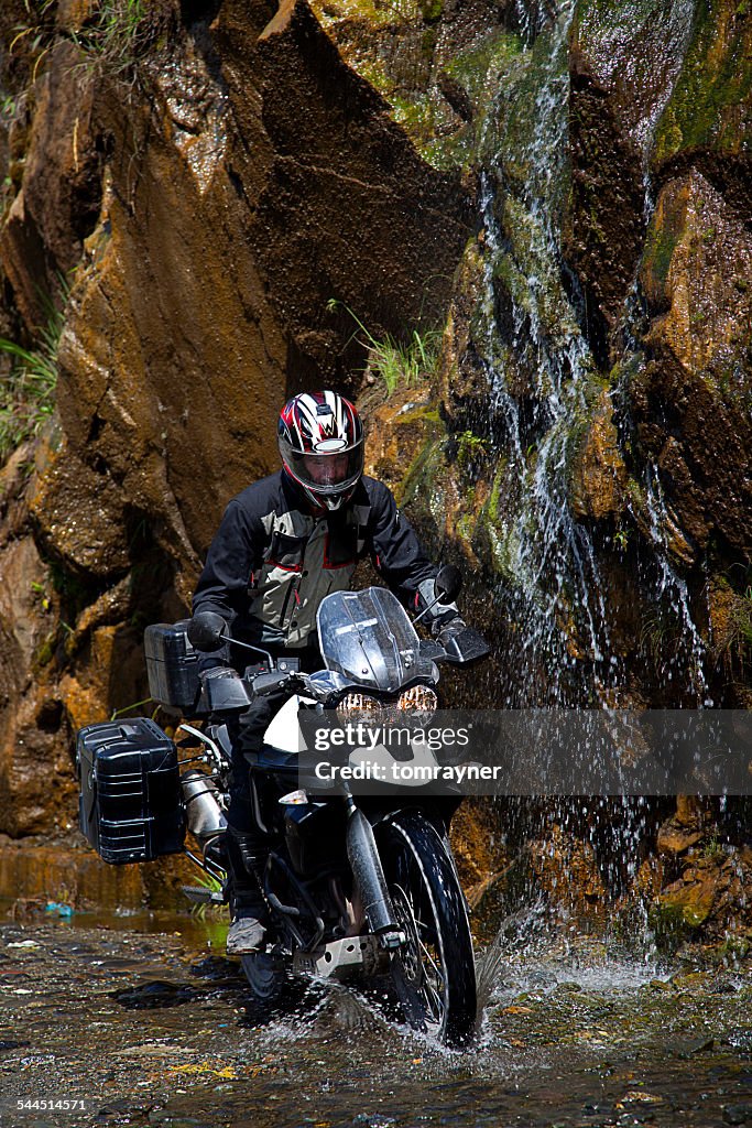 Ecuador, Man on motorcycle riding under waterfall