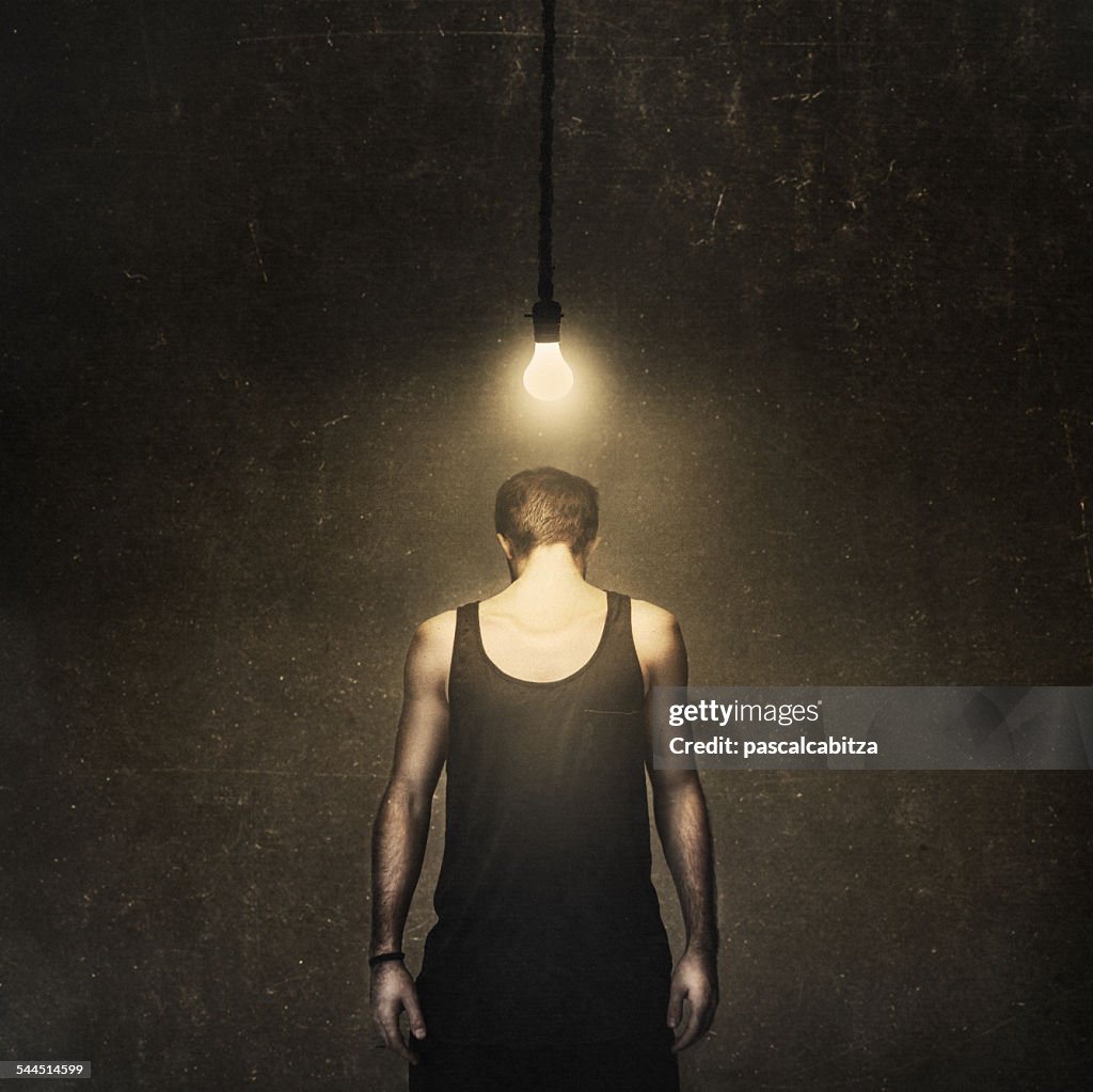 Front view of man standing under lightbulb with head turned around