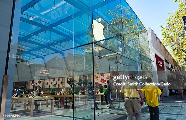 On a sunny day, two men--one wearing a Stanford University baseball cap--walk past the entrance to the flagship Apple electronics store on University...