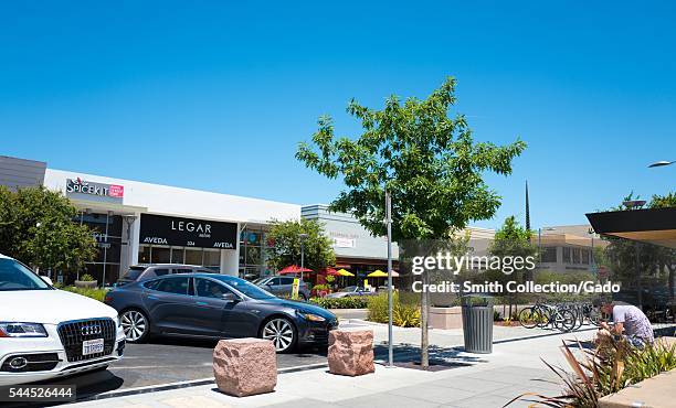 Along California Street on a sunny day in Palo Alto, a Tesla automobile pulls into a parking space while a young man sits and uses his smartphone,...