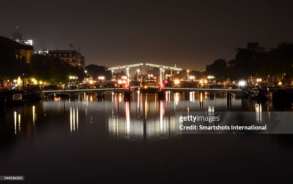 Magere Brug bridge illuminated at night and reflected on Amstel river in Amsterdam, Netherlands