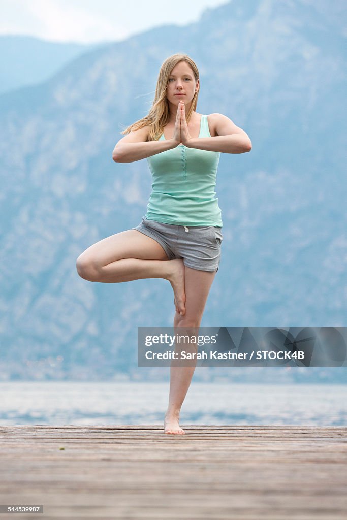 Woman practicing yoga on jetty at Lake Garda, Italy