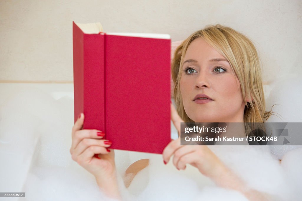 Blond young woman reading book in bathtub