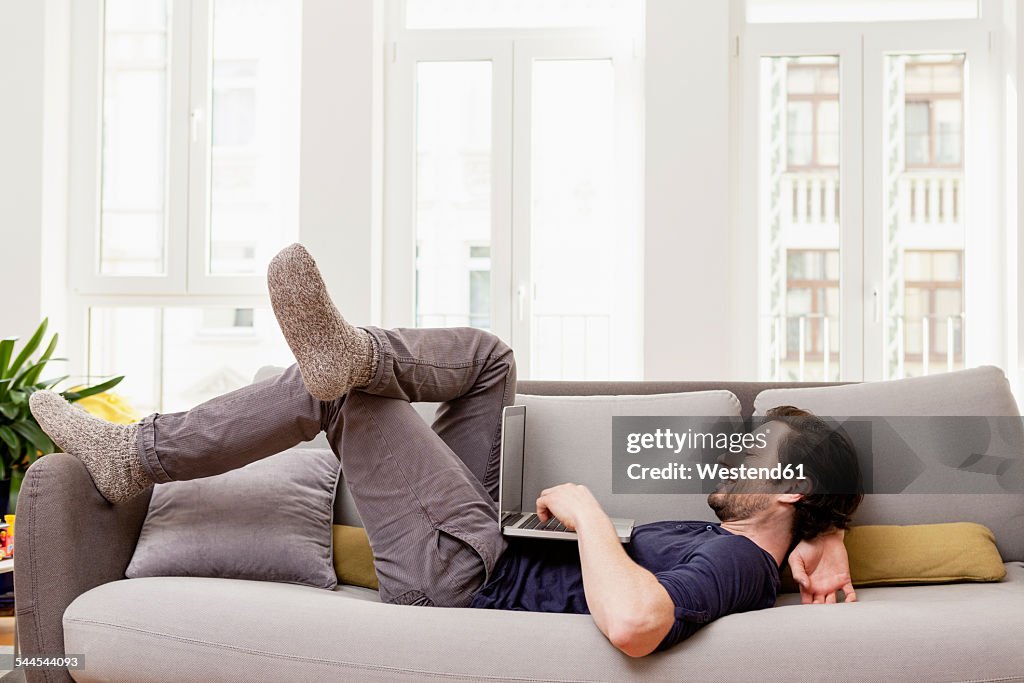 Relaxed man lying on couch using laptop