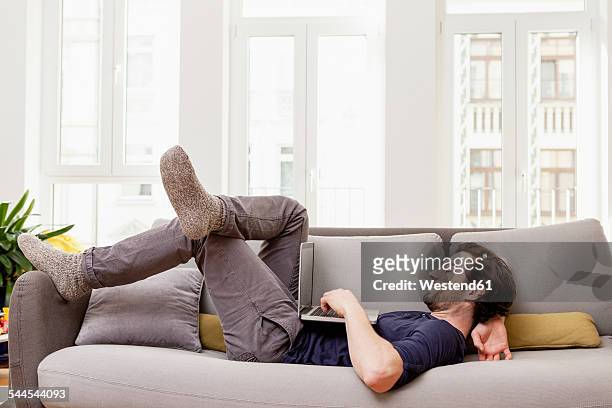 relaxed man lying on couch using laptop - reclining stock pictures, royalty-free photos & images