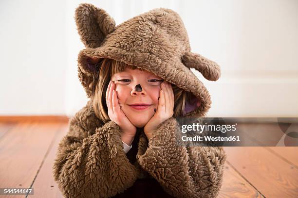 portrait of happy little girl masquerade as a bear lying on wooden floor - bear suit 個照片及圖片檔