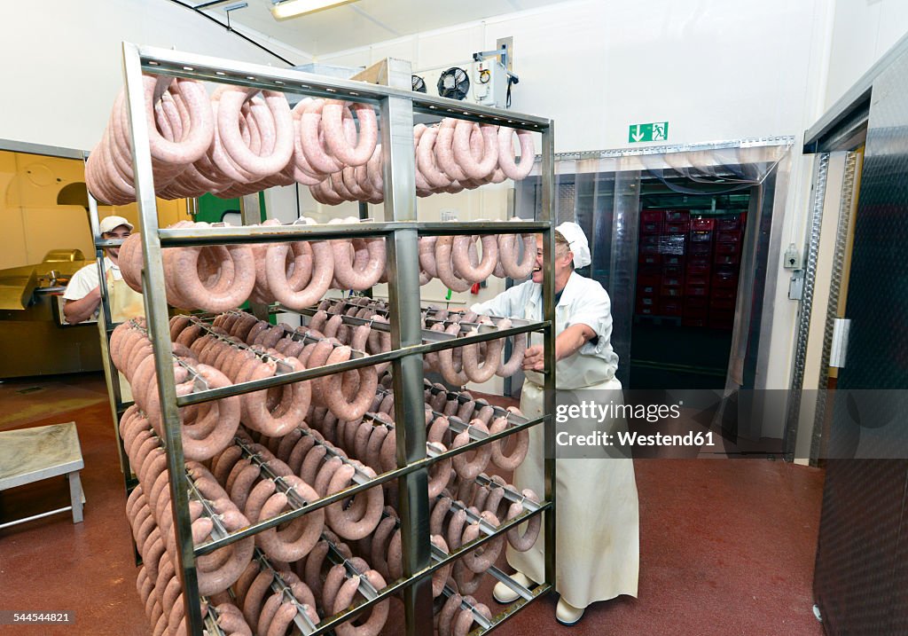 Woman in a butchery pulling rack with sausages for curing