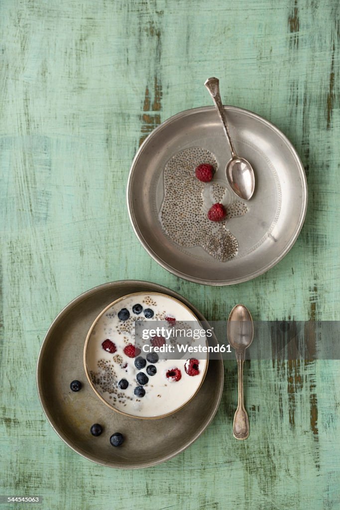 Metal bowl of vanilla yoghurt with chia, Salvia hispanica, blueberries and raspberries on green wood