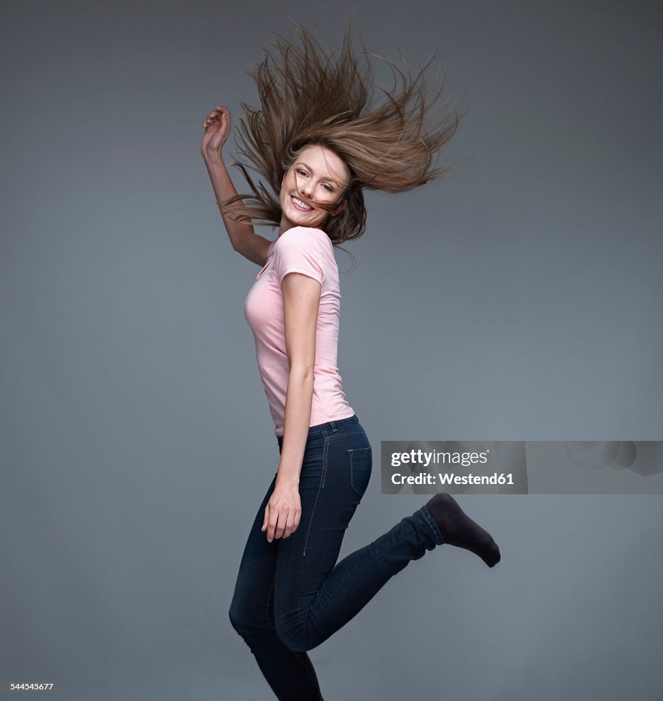 Portrait of smiling young woman dancing in front of grey background