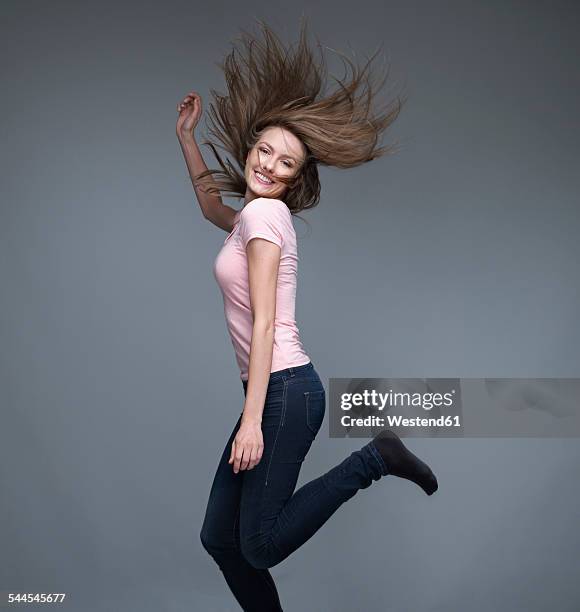 portrait of smiling young woman dancing in front of grey background - woman white t shirt stock pictures, royalty-free photos & images