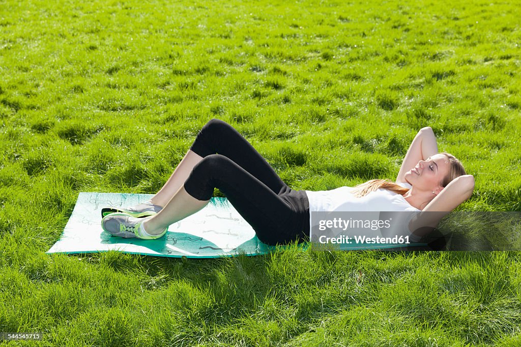 Teenage girl with gym mat lying on a meadow doing stretching exercises