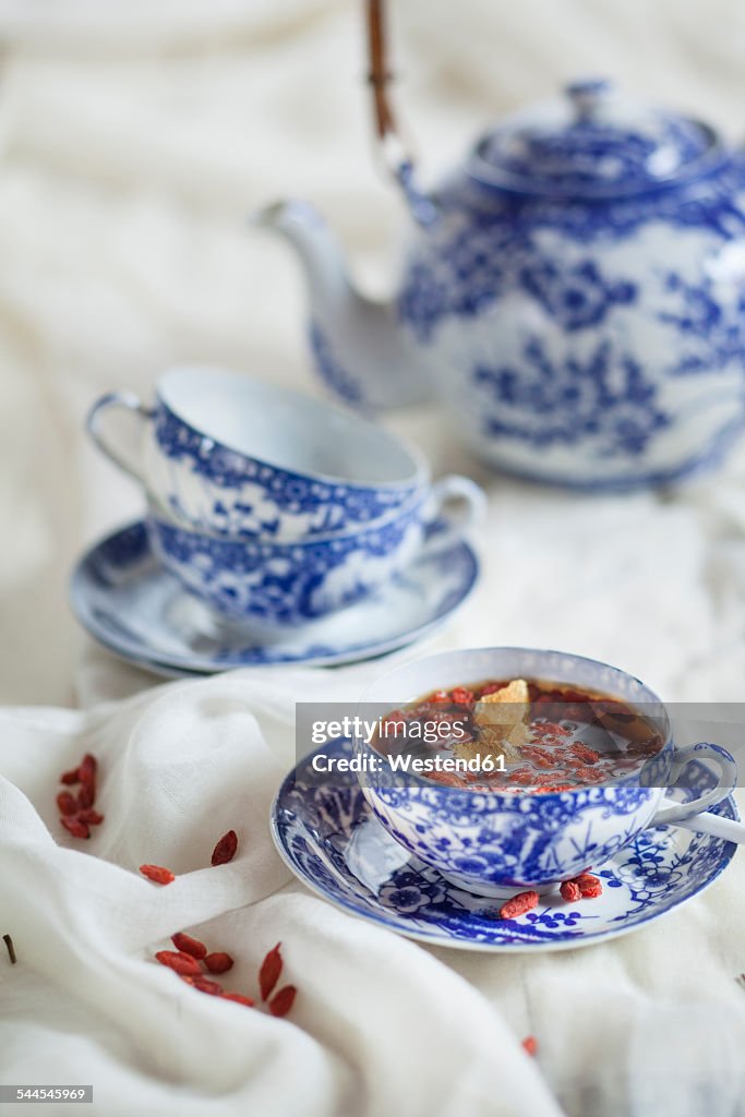 Cup of black spice tea with dried Goji berries, Lycium barbarum, on white cloth