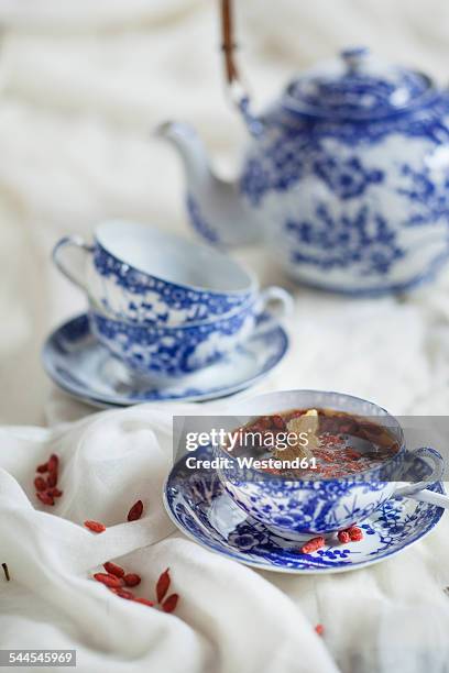 cup of black spice tea with dried goji berries, lycium barbarum, on white cloth - goji berry stock pictures, royalty-free photos & images