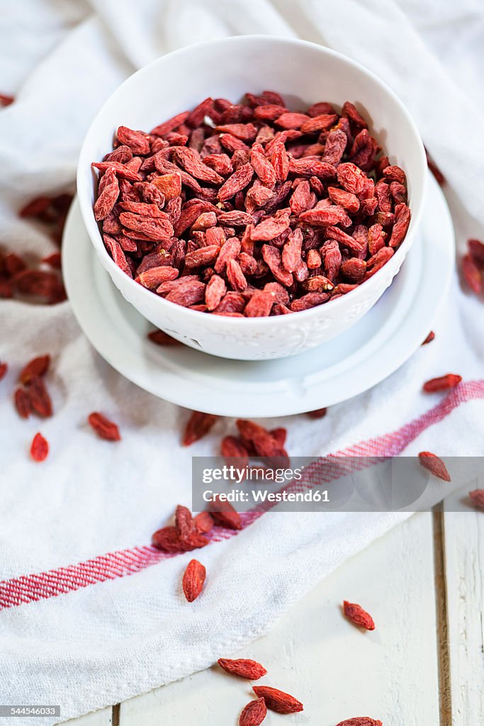 Bowl of Goji berries, Lycium barbarum, on kitchen towel and wood