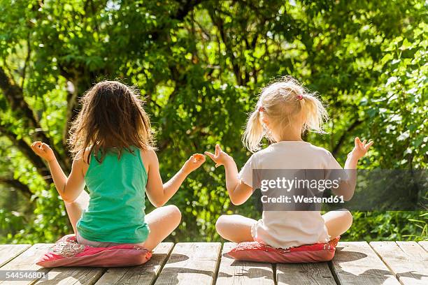 two relaxed girls sitting on wooden terrace - yoga kissen stock-fotos und bilder