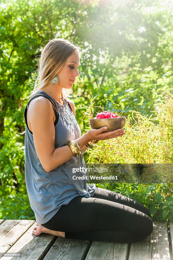 Woman holding bowl with blossom on wooden terrace