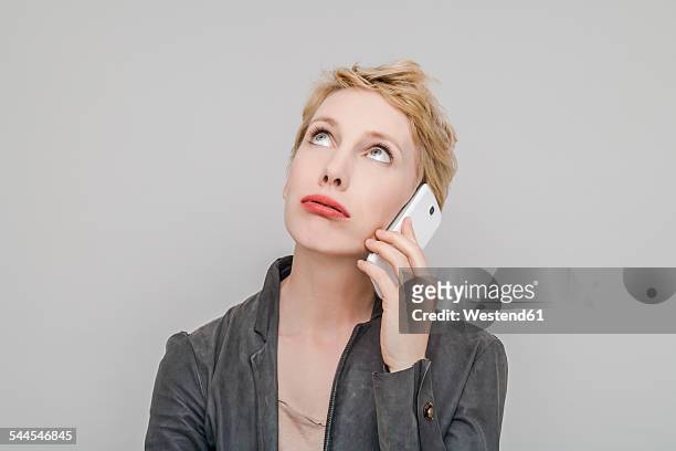 portrait of blond woman with smartphone pouting mouth looking up - wachten stockfoto's en -beelden
