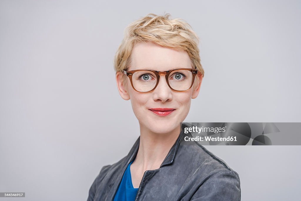 Portrait of smiling blond woman wearing glasses in front of grey background