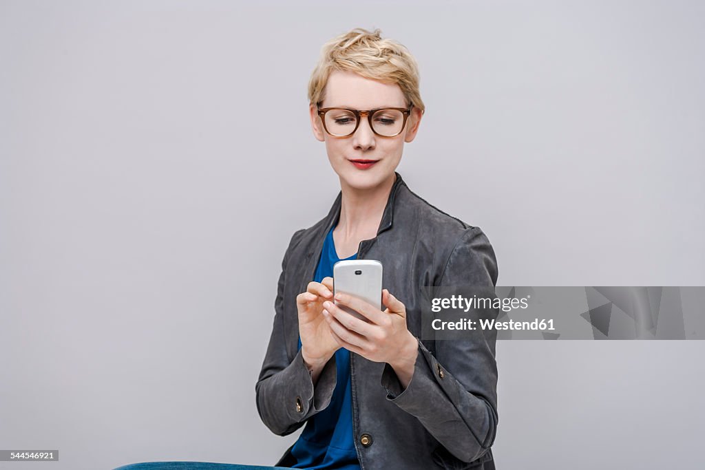 Portrait of smiling blond woman using smartphone in front of grey background