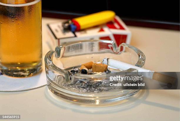 Rauchen in der Gaststätte. Auf dem Tresen / Tisch neben dem Glas Bier steht der Aschenbecher mit der qualmenden Zigarette.