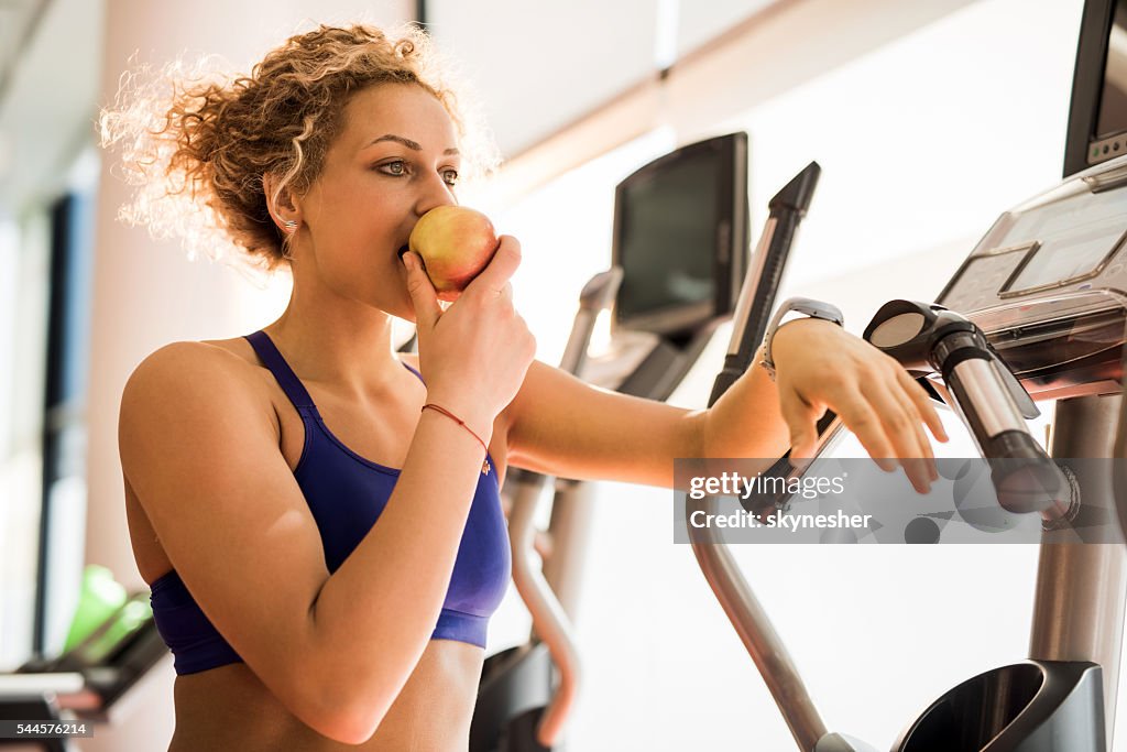 Athletic woman eating apple and in a gym.