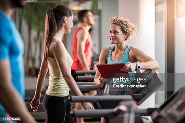 smiling fitness trainer talking to young woman in a gym. - female fitness instructor stock pictures, royalty-free photos & images
