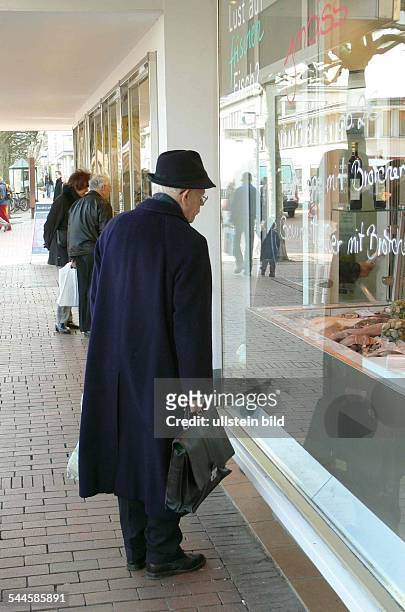 Deutschland, Nordrhein-Westfalen, Bonn, Älterer Mann mit Mantel und Aktentasche vor dem Schaufenster eines Fischgeschäftes