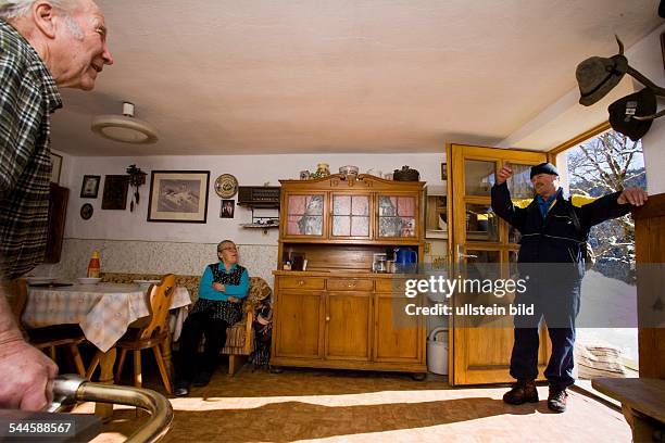 Deutschland, Bayern, Postzusteller auf der Eckbauer-Alm bei Garmisch-Partenkirchen. Postbote in der Wohnstube eines Bauernehepaares