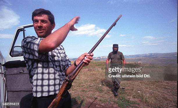 Russland, Tschetschenien - Tschetschenien-Konflikt - tschetschenischer Mann mit einem Gewehr, im Hintergrund Soldat einer tschetschenischen...