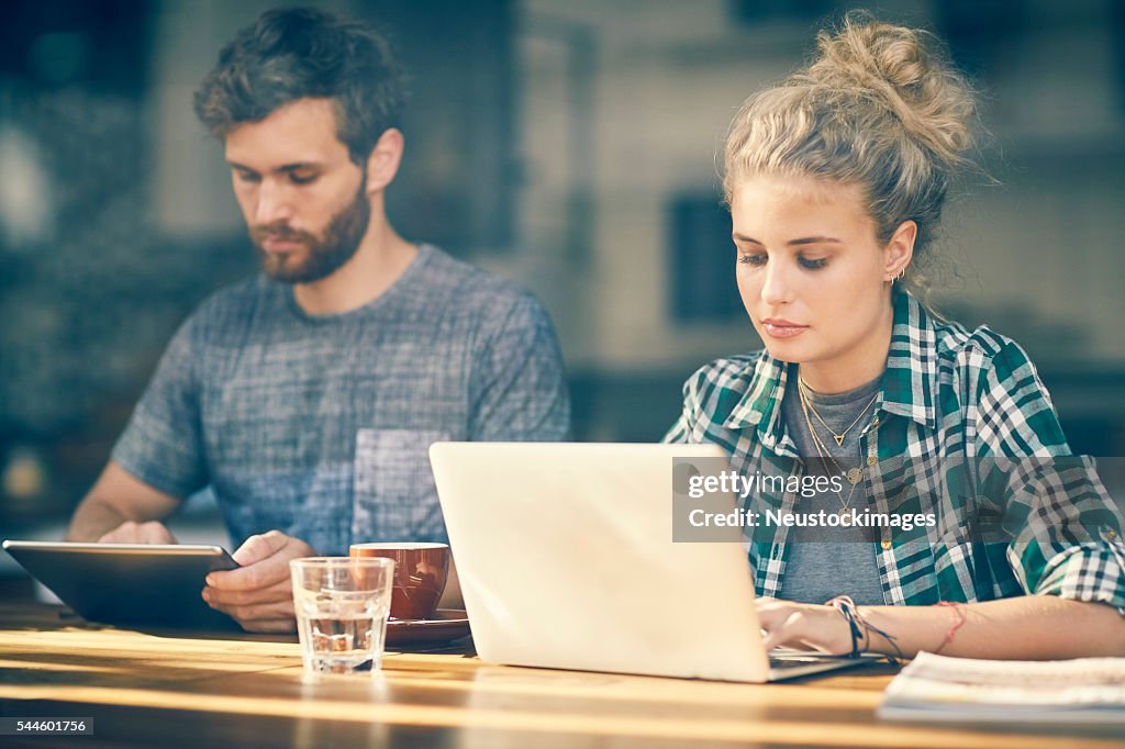 Bloguear comprimido Pareja joven en una computadora portátil en el interior de café de la ventana