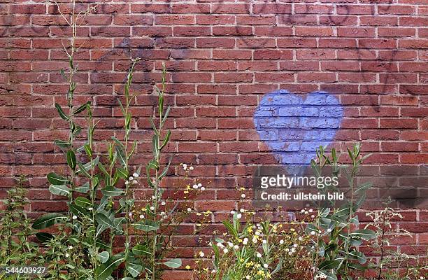 Rote Ziegelmauer mit einem gemalten blauen Herzen und wuchernden Wildpfanzen