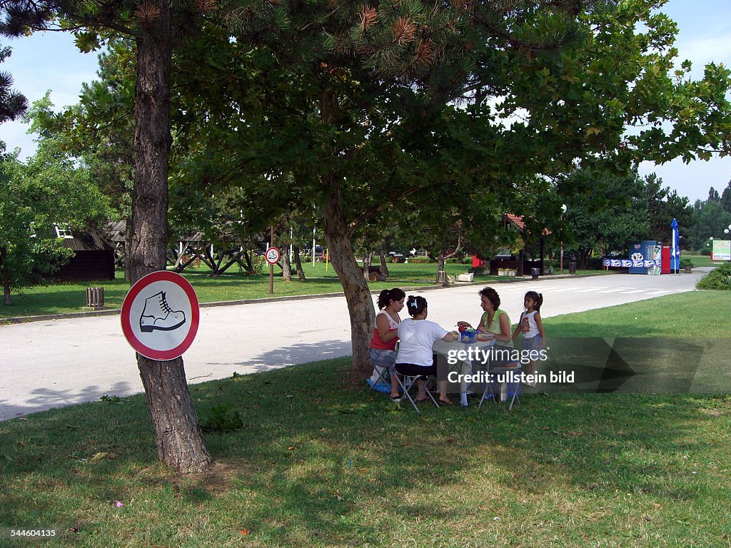 Croatia near Zagreb - family is sitting at a camping table on a green, in front on the sign an icon 'Keep off the grass'