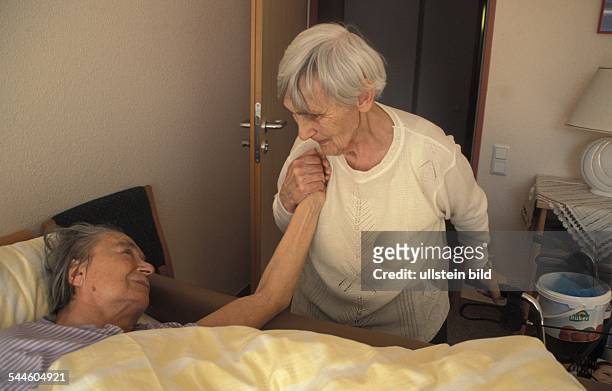 Deutschland , Berlin, - alte Frau im Altenpflegewohnheim "Dr.-Harnisch-Haus" am Bett einer anderen Heimbewohnerin-