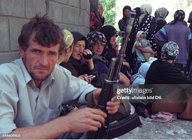 Russland, Tschetschenien, Grosny - Tschetschenien-Konflikt - tschetschenischer Mann mit Gewehr, im Hintergrund Frauen - August 2003