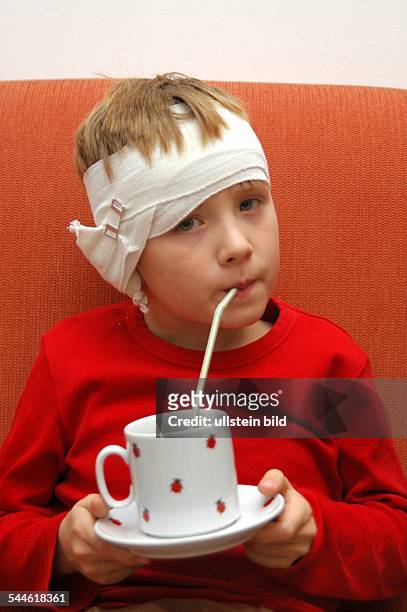 Hausmittel gegen Ohrenschmerzen, Junge mit Zwiebelsäckchen auf dem Ohr trinkt Tee mit einem Strohhalm !