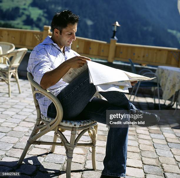 Mann beim ,Zeitung lesen auf einer Terrasse -vorhanden