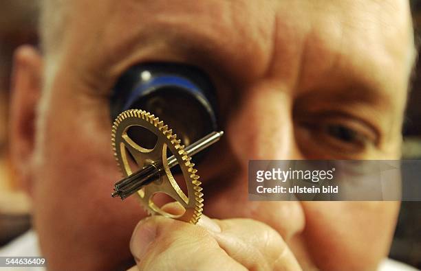 Deutschland, Handwerk , Uhrmacher betrachtet ein Zahnrad mit einer Lupe-