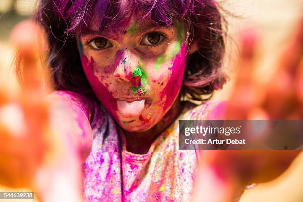 portrait of a little girl with tongue out showing his hands covered with colorful gulal powder during a holi party to give welcome to the springtime during a sunday family reunion. - holi portraits stock pictures, royalty-free photos & images