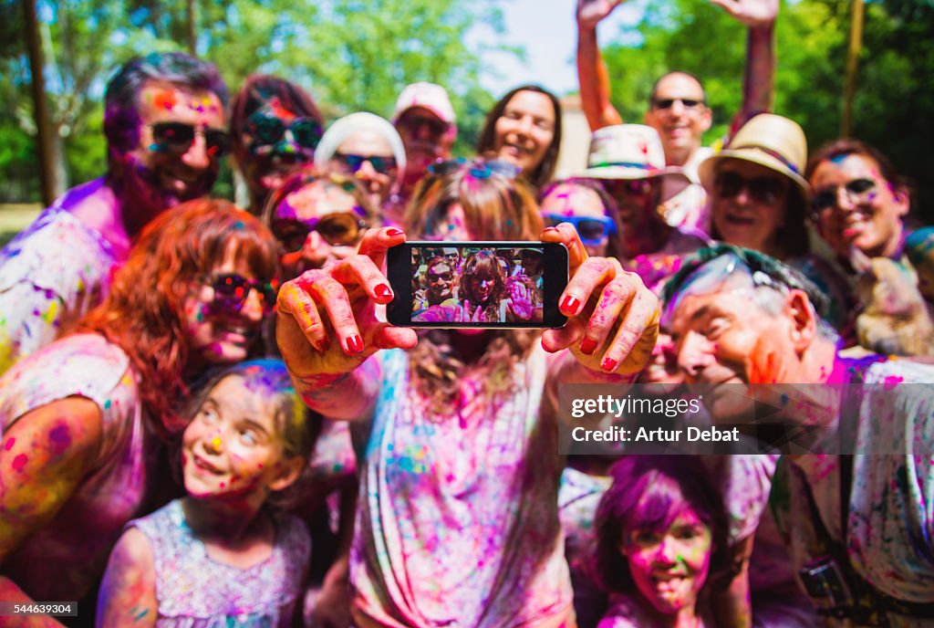 People taking a selfie together in group during a Holi celebration party in the outdoor with happiness expressions and covered with vivid colors.