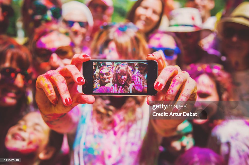 People taking a selfie together in group during a Holi celebration party in the outdoor with happiness expressions and covered with vivid colors.