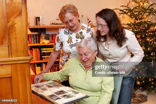 Deutschland, Familie zu Weihnachten, zum Jahreswechsel. Mutter, Tochter und Grossmutter betrachten im Wohnzimmer alte Familienfotos. Im Hintergrund...