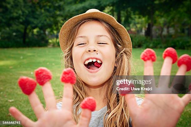 girl with raspberries on fingers, close up - child eating a fruit stock-fotos und bilder