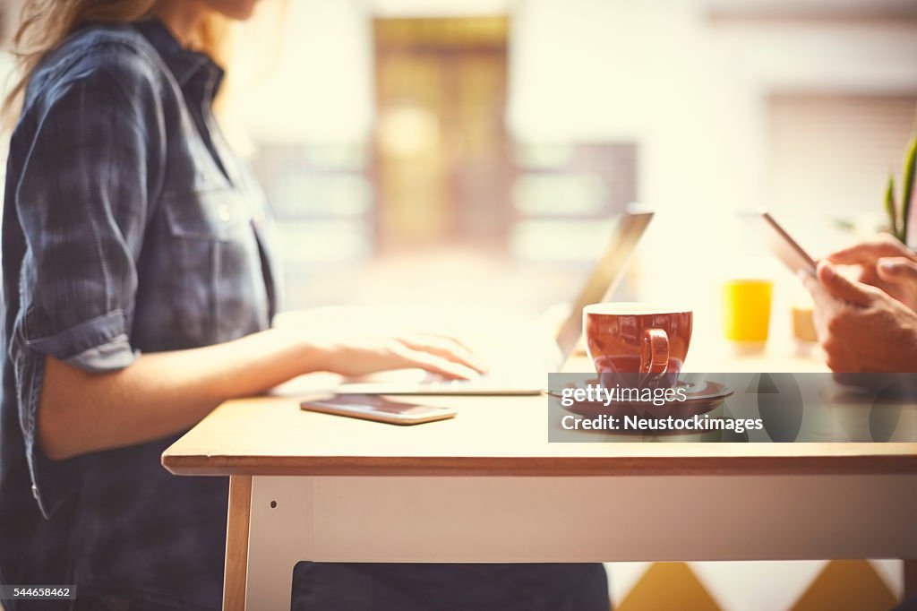 Midsection of woman using laptop at table in cafe