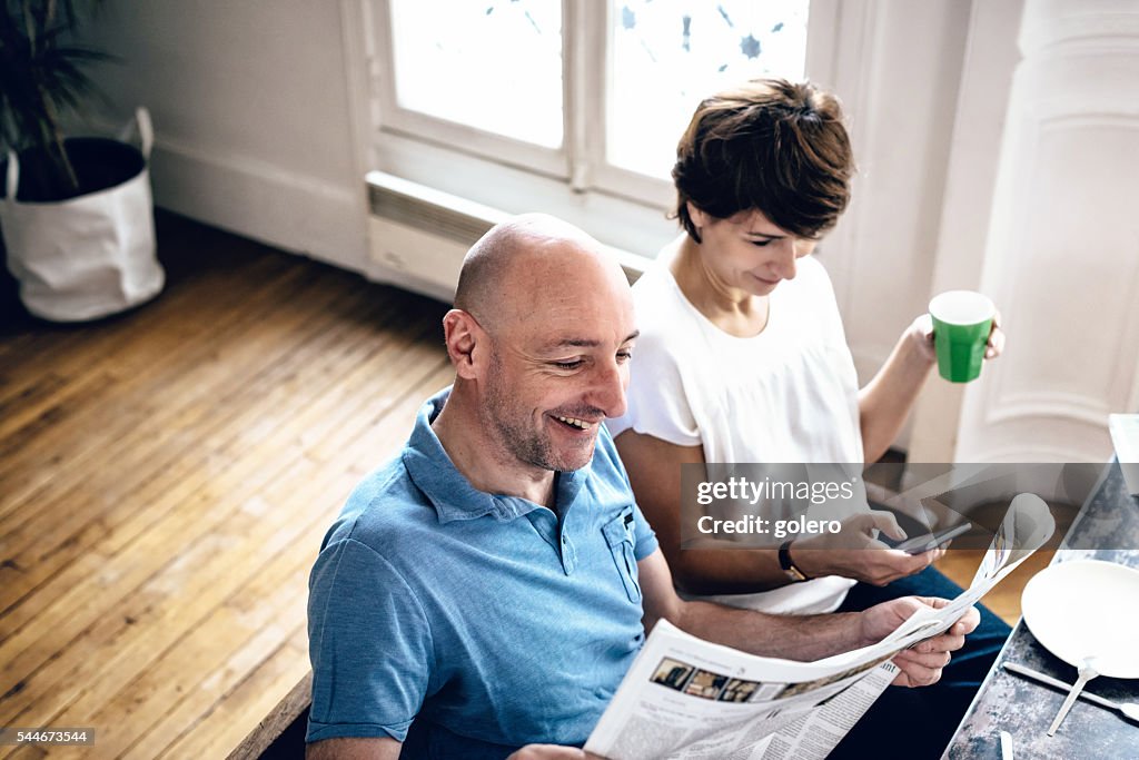 Beautiful midaged couple reading news in newspaper and on mobile