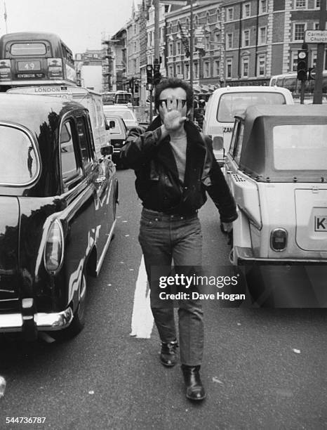 Singer Adam Ant covering his face as he angrily attempts to confront photographer Dave Hogan after getting out of a taxi, August 16th 1982.