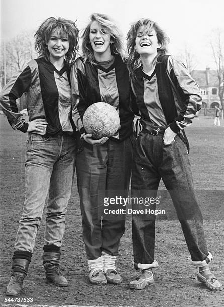 Portrait of pop band 'Bananarama', Keren Woodward, Sarah Dallin and Siobhan Fahey, wearing football shirts and standing in a field, March 16th 1983.