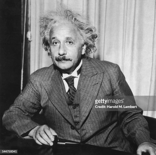 Portrait of physicist Albert Einstein, sitting at a table holding a pipe, circa 1933.