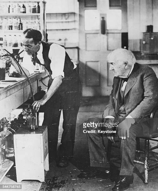 American inventor Thomas Edison watching his assistant George A Hart performing an experiment on rubber in their laboratory, West Orange, New Jersey,...