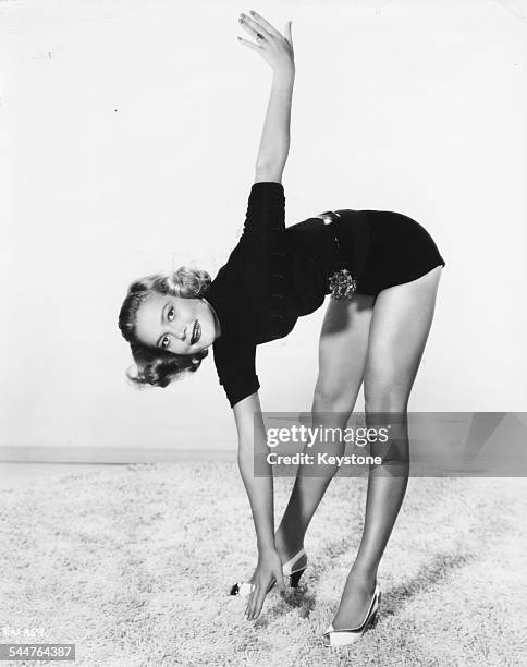 Portrait of actress Patrice Wymore touching her toes on the beach, as she gets in shape for her role in the movie 'The Big Trees', circa 1952.