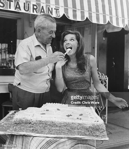 Film director William Wyler feeding cake to actress Samantha Eggar on her birthday, on the set of the film 'The Collector' in London, July 1st 1964.